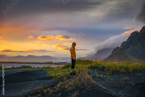 Tourist stands on a sand dune at Vestrahorn mountain in Iceland at sunset
