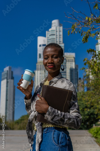 Photography a black Afro-American woman holding a notebook and a coffee, looking directly at