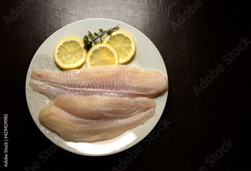 Panga fillets, Pterogymnus laniarius white fish from Asia, mild flavor with lemon slices and dark background photo