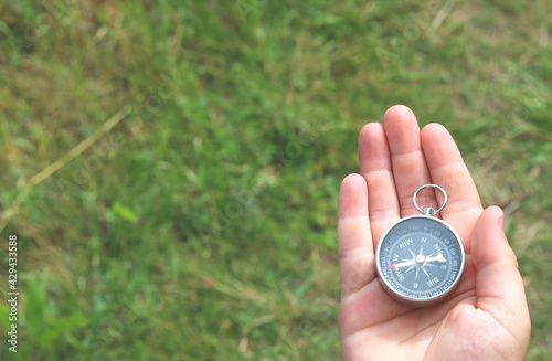 Old classic navigation compass in hand on natural background as symbol of tourism with compass, travel with compass and outdoor activities with compass