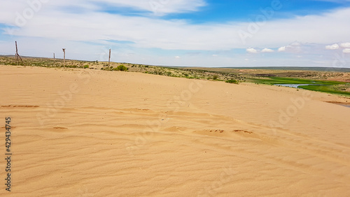 Hunshandake Desert in the nearby of Xilinhot, Inner Mongolia. The sand dunes are overgrown with a bit of grass. There is a small river in the middle. Blue sky with thick, white clouds. Solitude photo