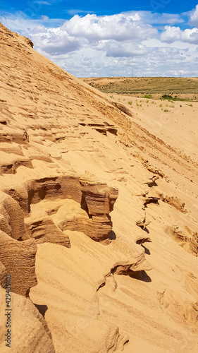 A close up on the wind shaped sides of a sand sune on Hunshandake Desert in the nearby of Xilinhot  Inner Mongolia. The sand dunes are overgrown with a bit of grass. Blue sky with thick  white clouds.