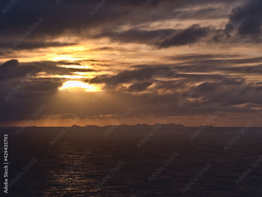 Stunning sunset above Atlantic ocean with dramatic sky of sun breaking through clouds with the silhouettes of Vestmannaeyjar islands on the horizon viewed from Dyrhólaey in southern Iceland.