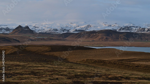 Stunning panoramic view of the snow-covered rugged foothills of Mýrdalsjökull glacier, covering volcano Katla, in evening sunlight viewed from Dyrholaey peninsula on the south coast of Iceland.