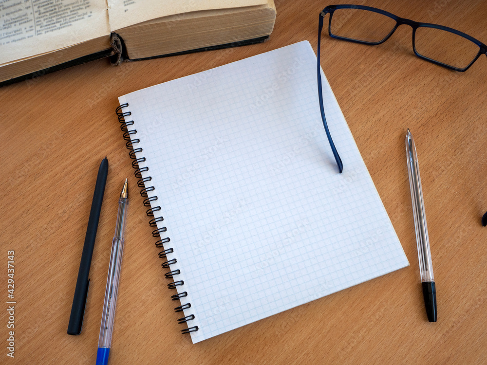 On a wooden table are a book, a notebook, pens and glasses. The concept of education, training, scientific work. On a wooden table are a book, a notebook, pens and glasses. The concept of education, training, scientific work.