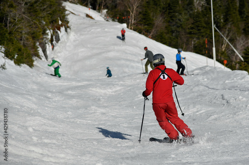 Stowe resort staff in red suit and Group of skiers seen from behind making a turn in Stowe Mountain resort in Vermont during Spring in mid-April warm sunny day.