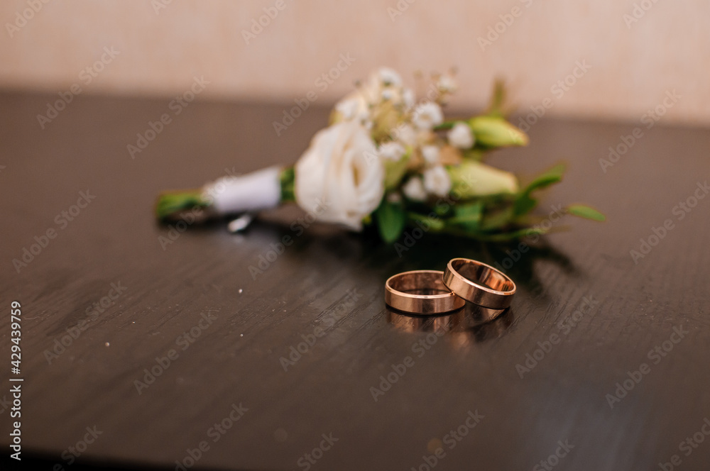 Pair of wedding gold rings and groom boutonniere on brown background Pair of wedding gold rings and groom boutonniere on brown background