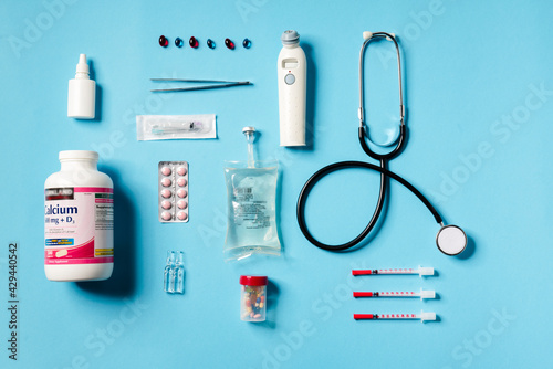 Overhead view of a medical instruments consisting of a jar of calcium, syringes, thermometer, stethoscope, tweezers lying on a blue background
