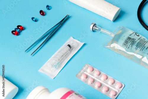 The close-up shot of a medical instruments consisting of tweezers, syringe, pills, liquid container lying on a blue background