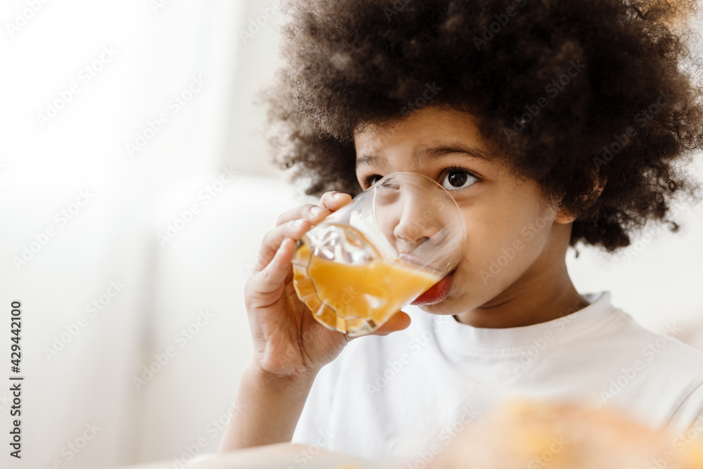 Black curly boy looking forward while drinking juice indoors Black curly boy looking forward while drinking juice indoors