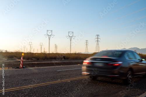 Electric pylons at sunset. Cars drive by on street. 