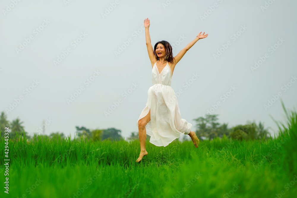lifestyle portrait of young attractive and happy Asian woman outdoors at green rice field landscape wearing elegant long dress jumping carefree in the air lifestyle portrait of young attractive and happy Asian woman outdoors at green rice field landscape wearing elegant long dress jumping carefree in the air