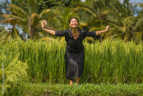 artistic portrait of young attractive and happy Asian woman outdoors at green rice field landscape dancing and doing relaxation body and mind yoga balance exercise 