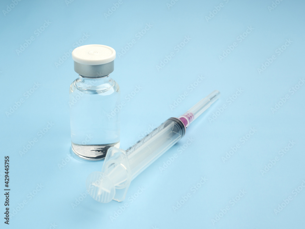 The vaccine in glass bottles with a syringe placed on a light blue background. Vaccine for immunization, and treatment from virus infection. Top view. Concept of medical and healthcar The vaccine in glass bottles with a syringe placed on a light blue background. Vaccine for immunization, and treatment from virus infection. Top view. Concept of medical and healthcar