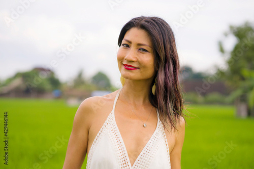 artistic portrait of young attractive and happy Asian woman outdoors at green rice field landscape wearing elegant long dress relaxed and carefree enjoying nature 