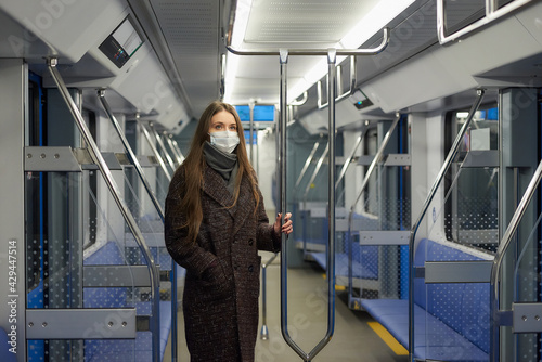 A woman in a medical face mask is keeping social distance in a modern subway car