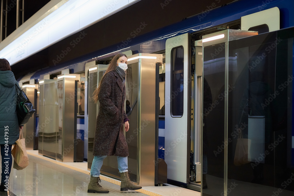 A girl in a surgical face mask is keeping social distance on a subway station.
