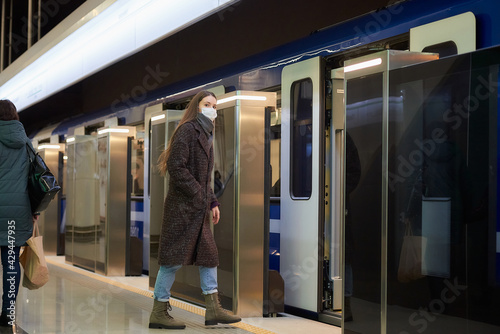 A girl in a surgical face mask is keeping social distance on a subway station.