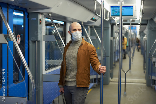 A bald man with a beard in a face mask is holding the handrail in a subway car. © Roman Tyukin