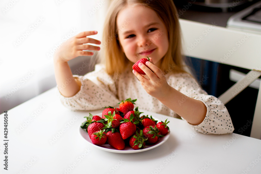 Cute little girl eating fresh strawberry in the kitchen. Healthy vitamin snack for kids. Ripe fresh berries. Harvest season. Natural vitamins . Cute little girl eating fresh strawberry in the kitchen. Healthy vitamin snack for kids. Ripe fresh berries. Harvest season. Natural vitamins .