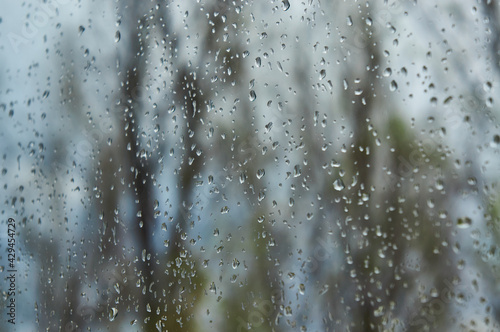 Rain drops falls on window glass with grey sky