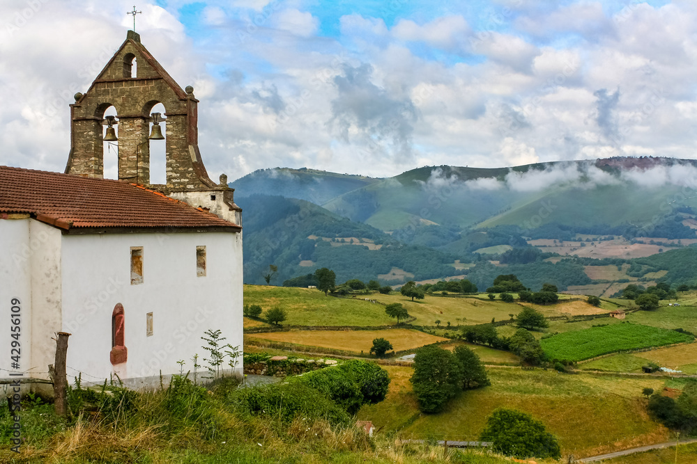Ancient church with bell tower in the green field with high mountains in the background. Asturias Spain