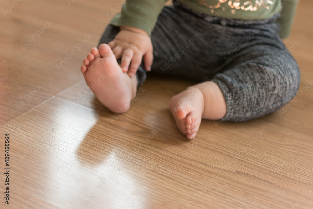Toddler baby sitting on laminate wood floor with bare feet; about to crawl away meeting a developmental milestone