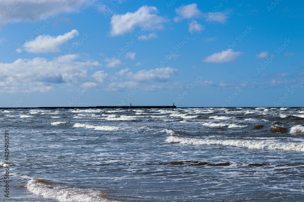 Sea waves under blue clody skies with pier in the distance