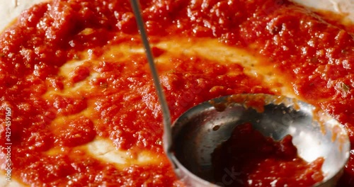 Chef is spreading tomato sauce on the pizza dough with a ladle. Cooker preparing traditional Italian pizza on professional kitchen - 4k footage