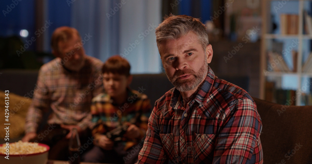 Father cheering up for his son playing computer console game with grandparent in living room. Concept for team, support and friendship. Entertainment.