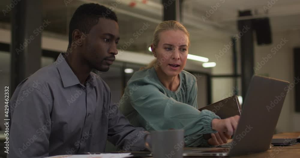 Diverse male and female business colleagues in discussion at work using laptop and tablet