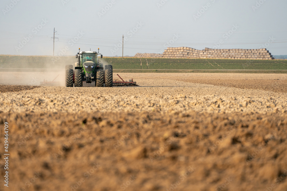 Obraz premium agricultural machinery works in the field. A tractor with a plow and a cultivator cultivates the land before sowing wheat and other cereals. The farmer plows the land very nicely and carefully.