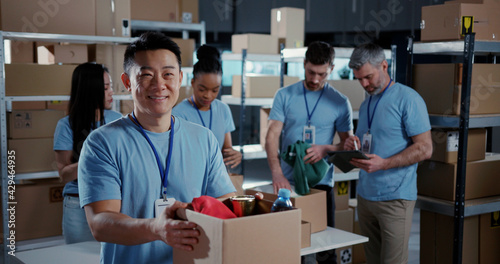 Multi-ethnic team of volunteers collaborating in workshop. Chinese male adult worker collecting food supply free delivery box smiling into camera. photo