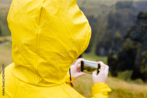 Tourist in yellow rain jacket taking picture with a phone of Iceland landsacepe