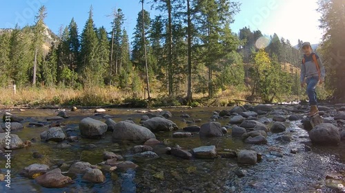 Small boy walking over the river stones in front of trees and mountains in Zakopane, Poland during autumn sunny day with beautiful sun.