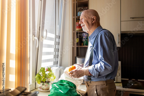 Senior man in kitchen at home looking out of window
