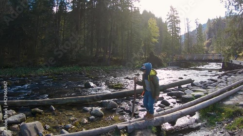 Small boy walking on tree logs over the river in front of trees and mountains in Zakopane, Poland during autumn sunny day with beautiful sun.