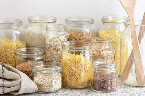 Variety of cereals, grains, pasta, seeds in glass jars uncooked on white kitchen background, closeup, zero waste, eco friendly, balanced diet food, healthy clean eating concept