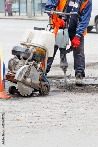 A road worker repairs a section of road with an electric jackhammer and gas cutter.