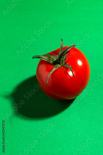 Red ripe fresh tomato on a green paper background.