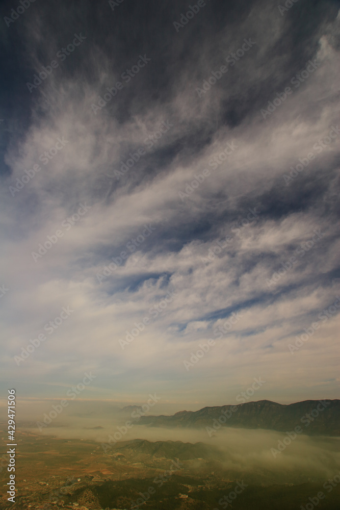 Cielo nuboso con cirros al amanecer, sobre valle y montaña con niebla. Sierra y Campo de Ricote, Sierra del Oro y Cagitán. Murcia (España).