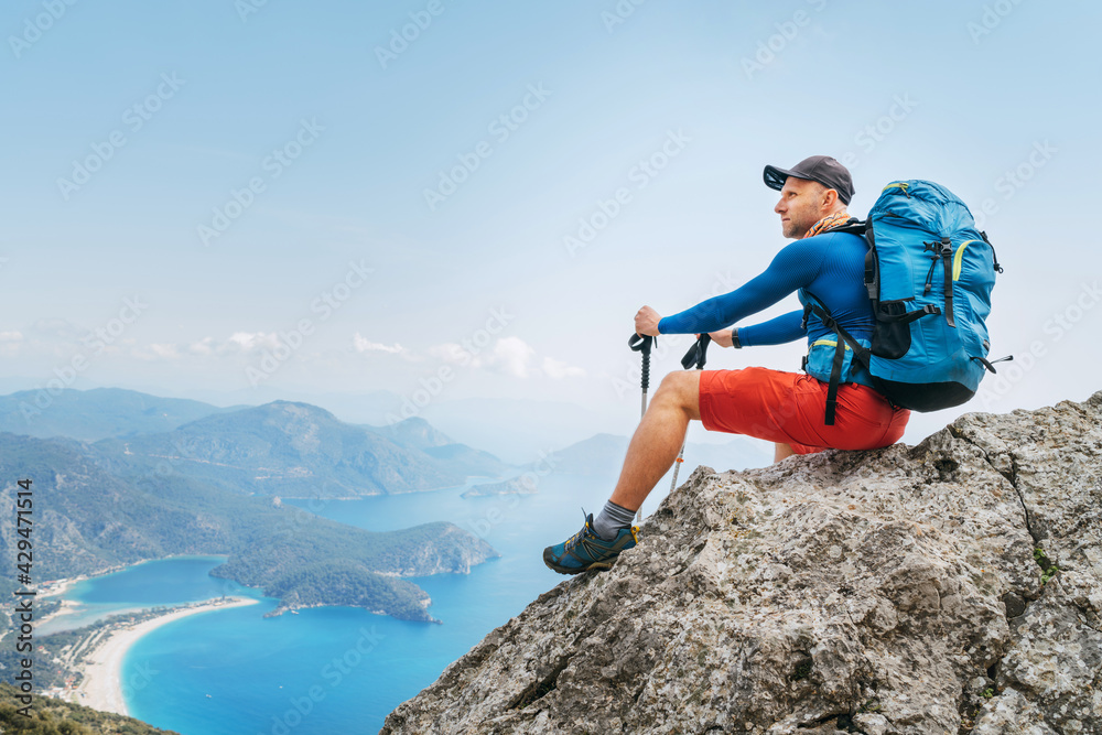 Young backpacker man sitting on cliff and enjoying the Mediterranean Sea bay at during Lycian Way trekking walk. Famous Likya Yolu Turkish route. Active sporty people vacations concept image