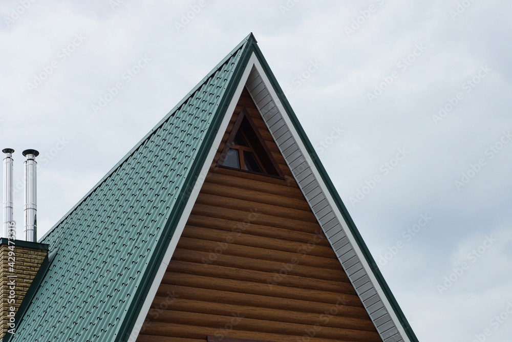 brown wooden attic of a private house with a small window under a green tiled roof against a gray sky