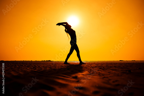  Young healthy Silhouette woman practicing yoga on the beach at sunset. Fitness  meditation  and a healthy lifestyle.