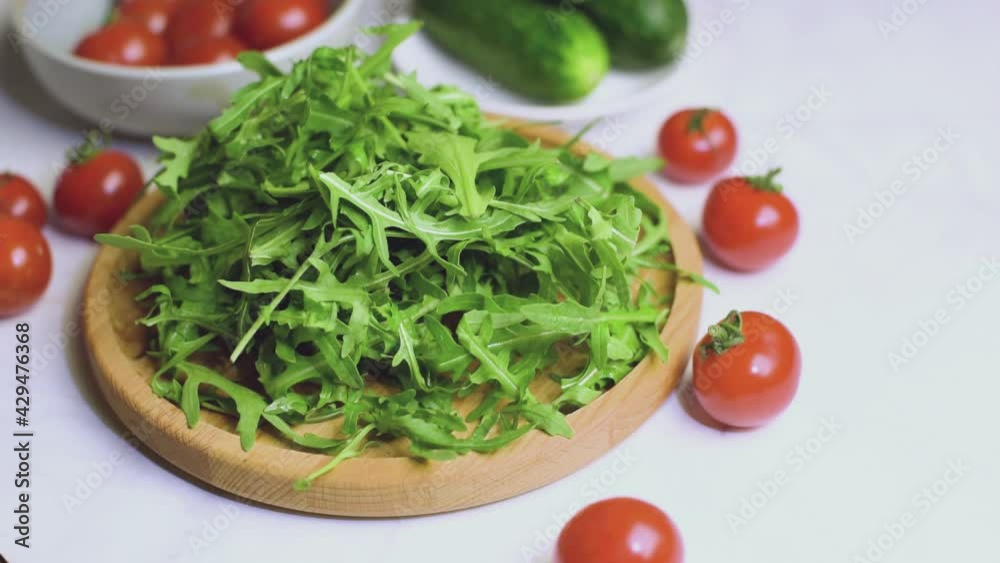 Fresh organic arugula leaves falling on on wooden plate for cooking salad. Fresh organic arugula leaves falling on on wooden plate for cooking salad.