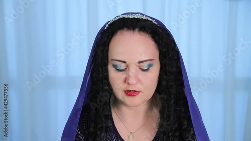 A Jewish woman with a cape on her head reads a blessing after lighting candles on Shabbat. Medium plan photo