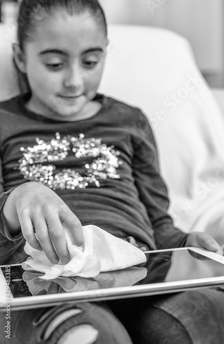 Young girl throughly cleaning tablet in covid pandemic photo