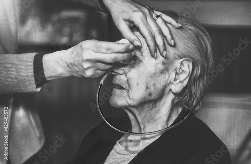 Giving medical eye drops to elderly woman in delicate health conditions