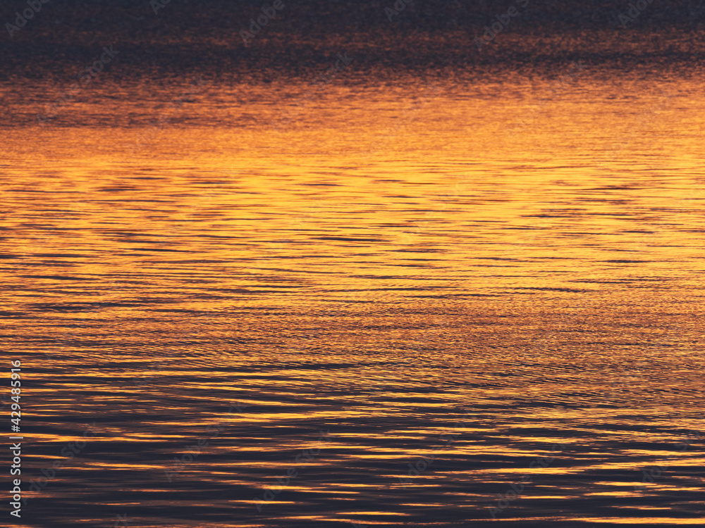 Small waves on water surface in the rays of the rising sun as background