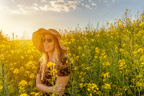 Woman in straw sun hat enjoying spring in yellow flowers field.Summer concept lifestyle female against sunset golden light in nature .
